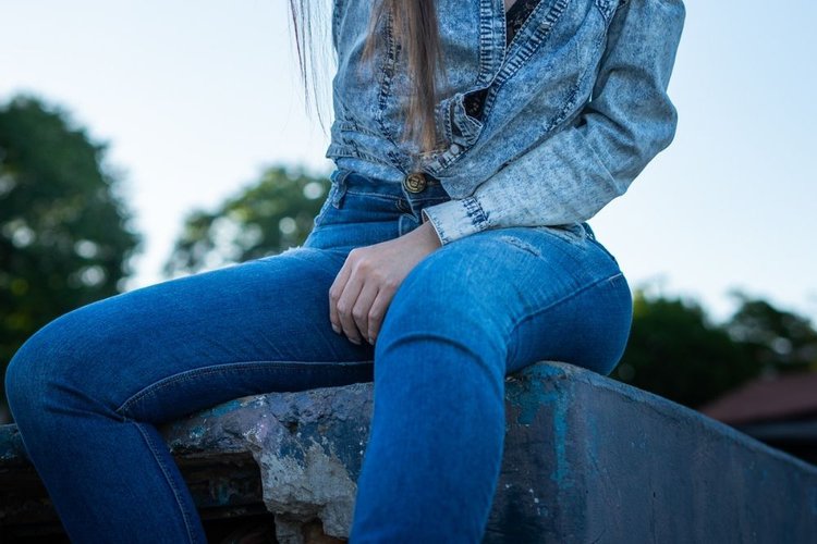 Women wear jeans and sit on the rock