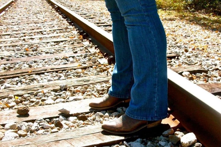 Women wear jeans with cowboy boots standing on the train tracks