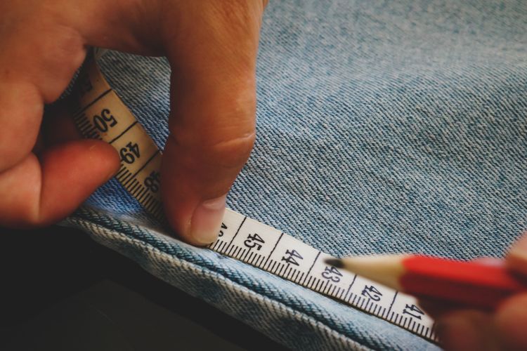 a tailor measures the seam of jeans