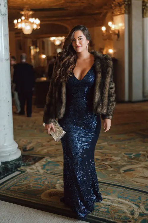 A curvy woman wears a midnight blue sequin gown with full-length sleeves and a mermaid cut, paired with a faux fur jacket and metallic clutch