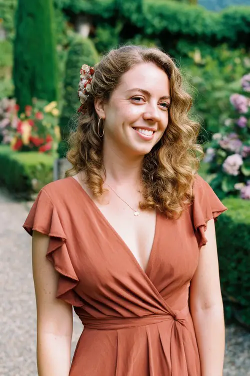 A curvy woman wears a wrap-style tea-length dress in terra cotta with subtle ruffle details and a floral scarf