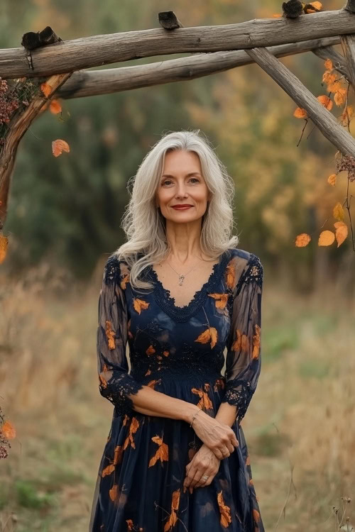 A fashionable woman over 50 in a navy dress with autumn leaf motifs, posing near a wooden wedding arch