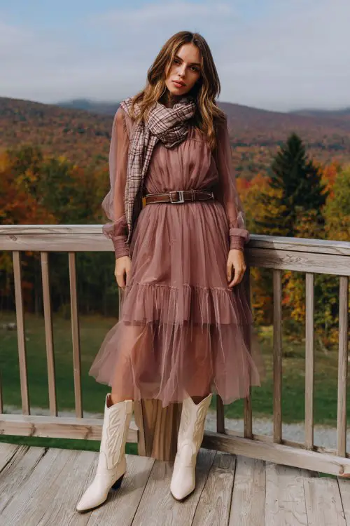 A layered tulle midi dress in dusty rose with a sheer long-sleeve overlay, cinched at the waist with a leather belt, paired with vintage cream cowboy boots