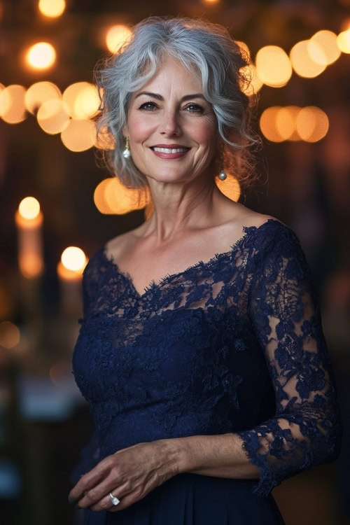 A stylish woman over 50 in a navy dress with lace sleeves, smiling confidently in a candle-lit evening wedding scene