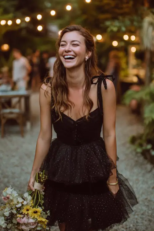 A woman in a black tulle tea-length dress with layered ruffles and embroidered polka dots