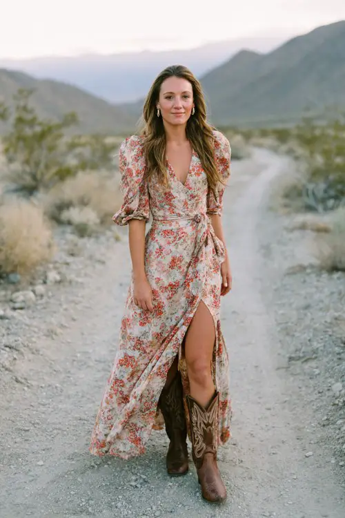 A woman over 30 wears a floral print maxi dress with a front slit and brown cowboy boots