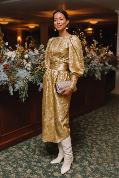 A woman over 30 wears a gold brocade dress with a boxy silhouette and ivory heeled boots, accessorized with drop earrings and a velvet clutch (3)