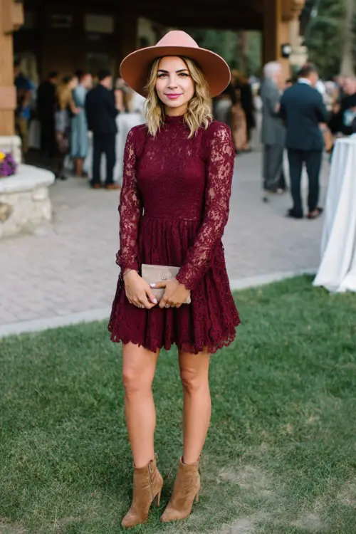 A woman over 40 in a burgundy lace fit-and-flare dress paired with suede ankle boots and a wide-brim hat