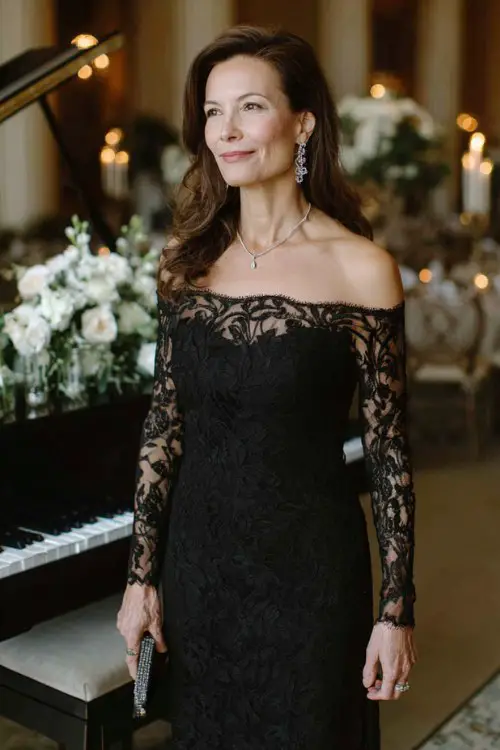 A woman over 40 wears a long-sleeve black gown with lace detailing and silver accessories