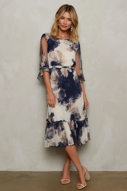 A woman over 50 wearing a navy and ivory floral print midi dress, paired with block heels and pearl earrings