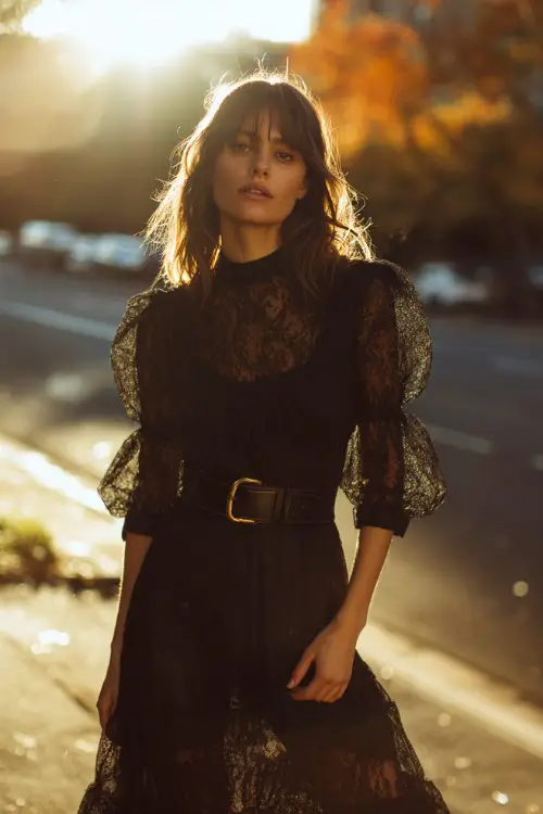 A woman wears a black lace dress with sheer bishop sleeves, paired with ankle boots and a wide leather belt