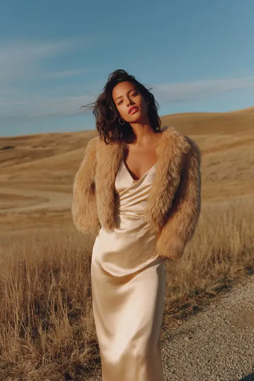 A woman wears a champagne-colored satin wrap dress, topped with a cropped faux-fur jacket