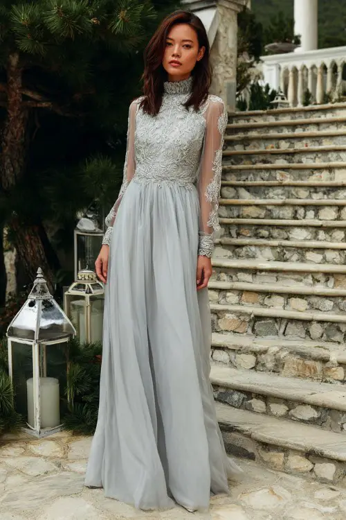 A woman wears a high-neck long-sleeved gown in soft silver with intricate embroidery on the bodice and sheer sleeves