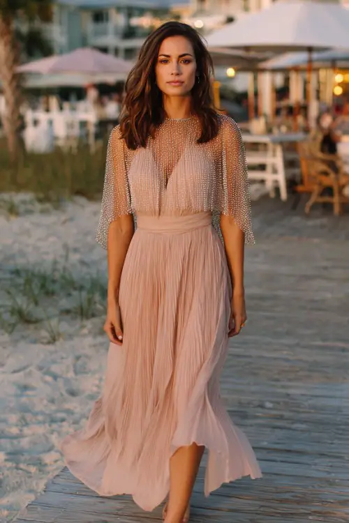 A woman wears a rose gold midi dress with layered pleated chiffon and a sequin-covered capelet