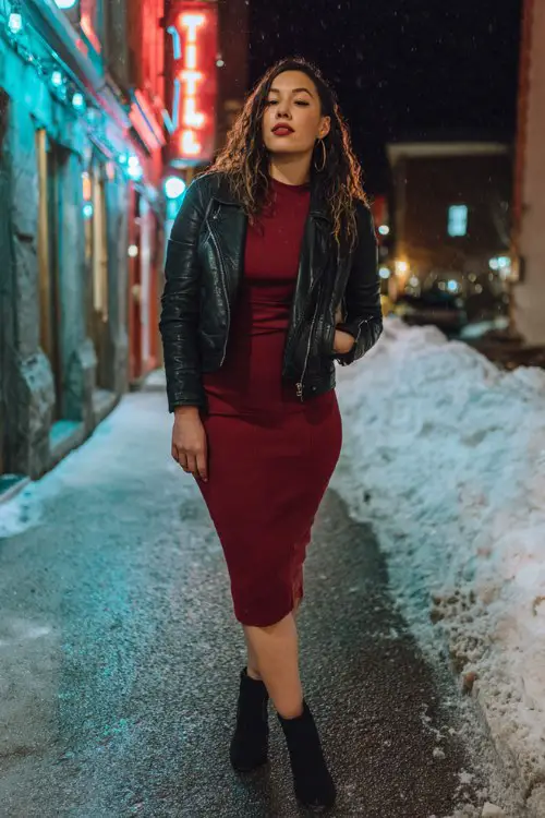 A curvy woman in a black leather jacket layered over a burgundy bodycon midi and ankle boots