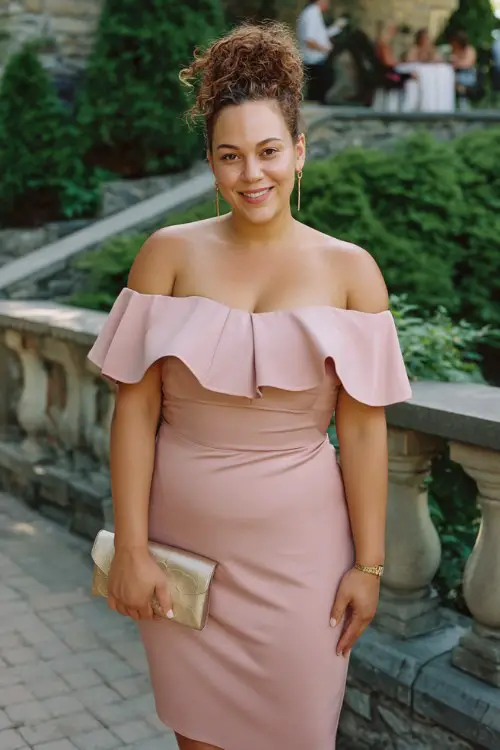 A curvy woman wears a rose pink midi dress with a tulip hem and off-the-shoulder ruffle detail