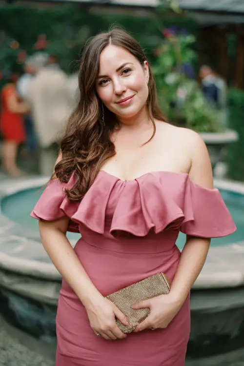 A curvy woman wears a rose pink midi dress with a tulip hem and off-the-shoulder ruffle detail