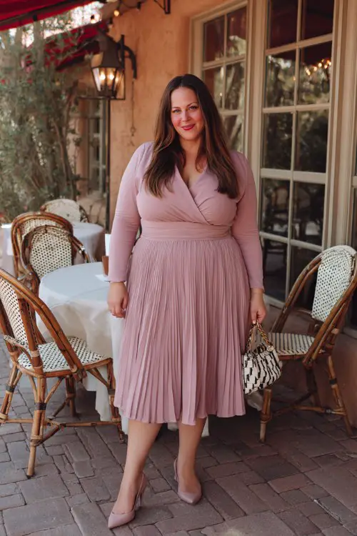A plus-size woman over 30 wears a flared wrap top with long sleeves and a pleated midi skirt in dusty rose, paired with kitten heels