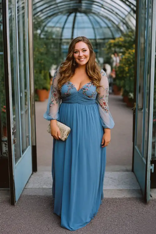 A plus-size woman wears a cornflower blue gown with an empire waist, pleated skirt, and sheer bishop sleeves embroidered with tiny florals