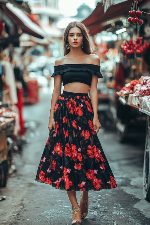 A woman in a black off-the-shoulder top, a flowy midi skirt with red floral prints, and ballet flats