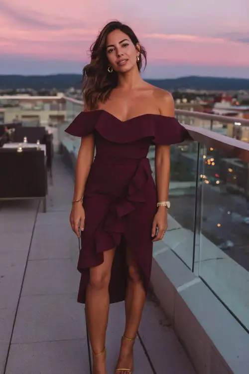 A woman over 30 wears a deep burgundy off-the-shoulder bodycon dress with a dramatic ruffled slit and gold stilettos