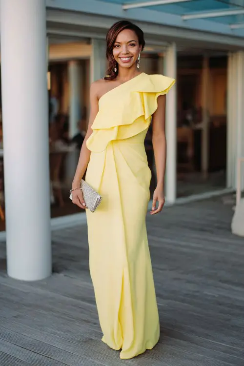 A woman over 30 wears a lemon yellow one-shoulder gown with an asymmetrical ruffle and pleated skirt
