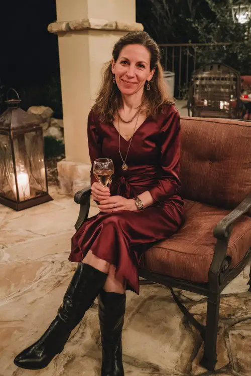A woman over 40 wears a burgundy fit-and-flare dress with subtle shimmer and pointed black leather boots