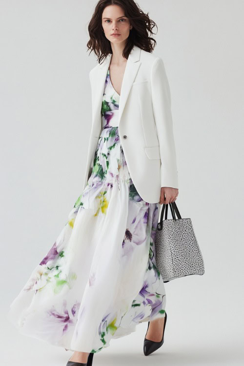 A woman wearing a white tailored blazer over a floral maxi dress, styled with a structured handbag and loafers