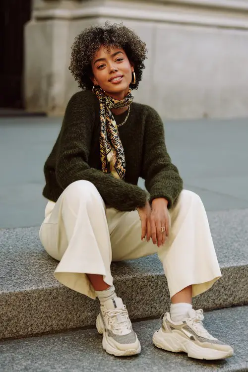 A woman wears a deep forest green cropped knit sweater with wide-leg cream trousers and chunky sneakers