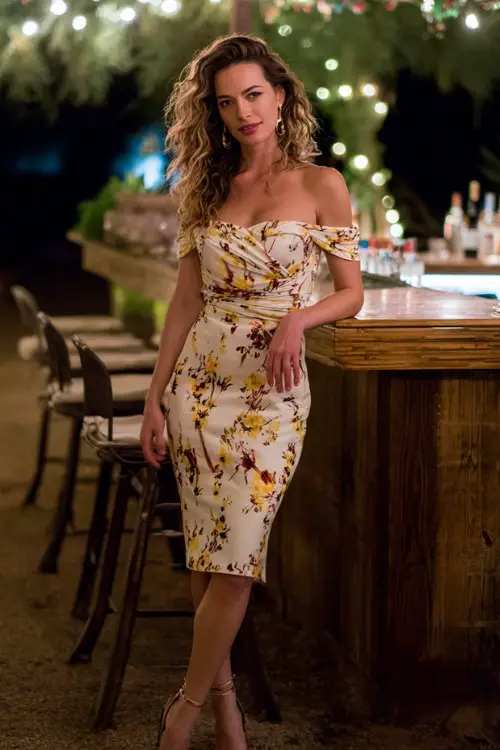 A woman wears a fitted off-shoulder floral dress with soft curls and strappy heels