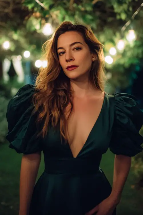 a woman wearing a dark emerald green dress with dramatic puff sleeves and a deep V neckline