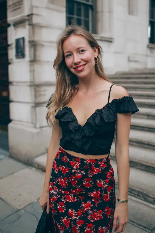 a woman wears a ruffle top with black midi skirt with red floral patterns for date night