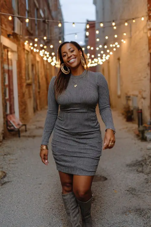 A curvy Black woman wears a fitted ribbed knit dress with knee-high boots and gold hoop earrings