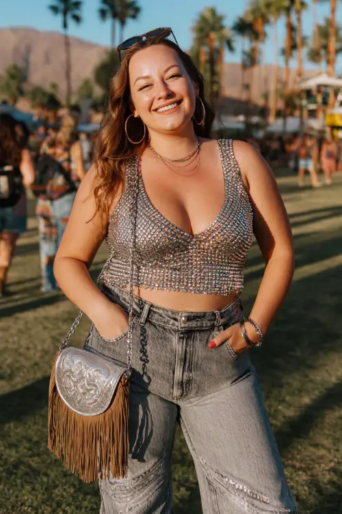 A plus-size woman wears silver cowboy boots with high-waisted flare jeans and a rhinestone mesh crop top layered over a bralette