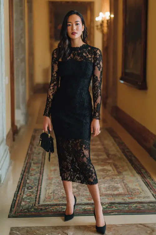A woman wears a black lace midi dress with sheer sleeves and a defined waist, paired with elegant heels