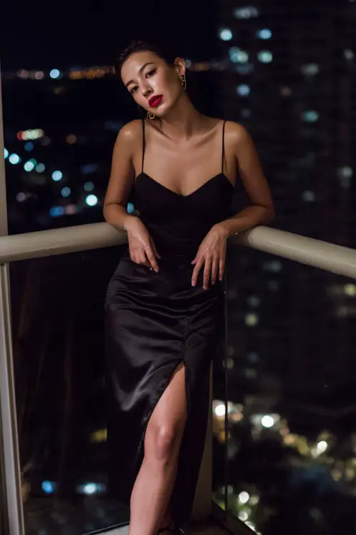 A woman wears a fitted black camisole tucked into a high-slit satin skirt, paired with strappy heels and a bold red lip