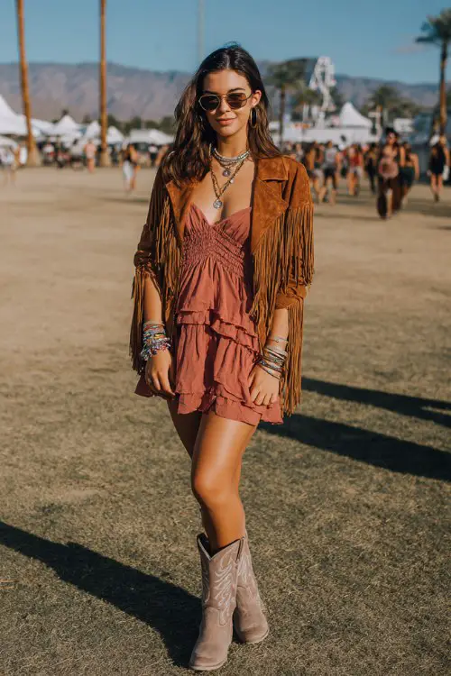 A curvy woman wears dusty rose cowboy boots with a ruffled boho mini dress layered under a suede fringe jacket, accessorized with stacked bracelets and layered necklaces