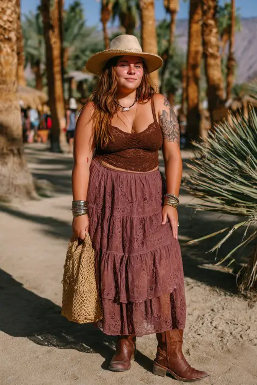 A plus-size woman wears brown cowboy boots with a tiered boho maxi skirt and a fitted lace camisole, accessorized with stacked bangles