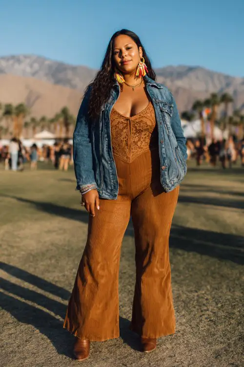 A plus-size woman wears brown cowboy boots with high-waisted flare jeans and a fitted lace bodysuit, layered with an oversized denim jacket