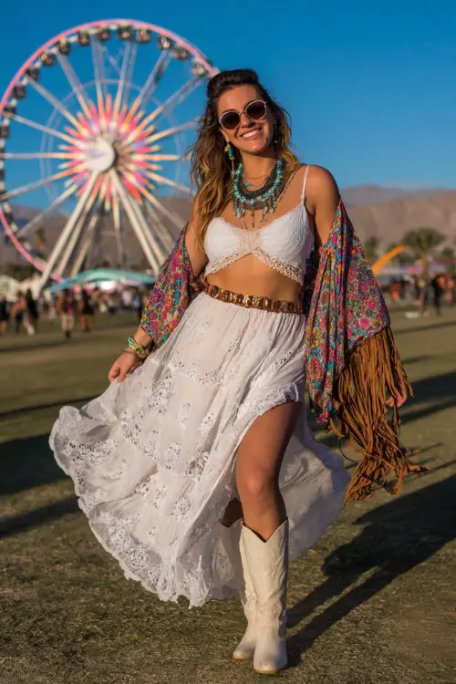 A plus-size woman wears white cowboy boots with a flowing embroidered maxi skirt and crochet crop top, layered with a dramatic fringe kimono and stacked turquoise necklaces