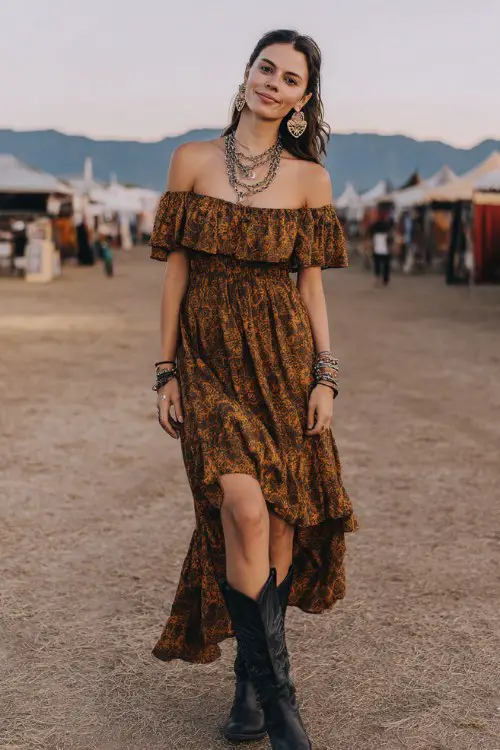 A woman wears black cowboy boots with a breezy off-shoulder maxi dress in earthy tones, accessorized with statement earrings