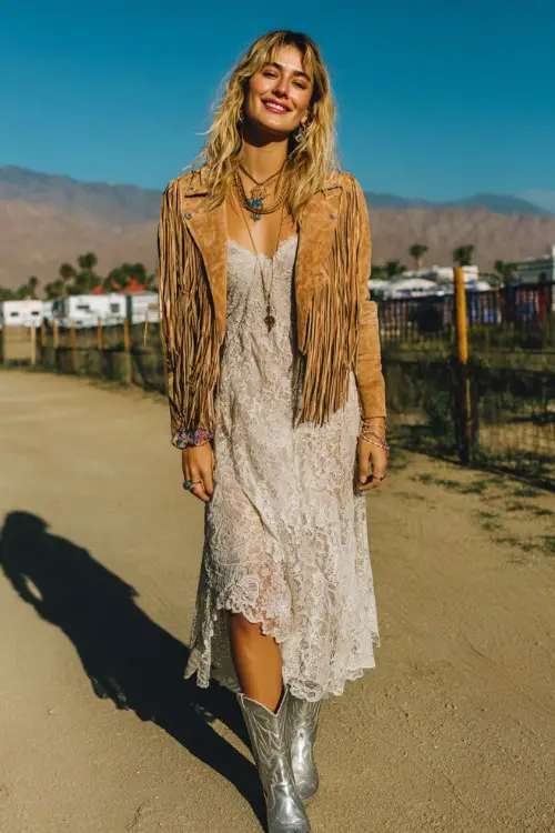 A woman wears metallic cowboy boots with a dreamy lace midi dress and suede fringe jacket, styled with bold rings and layered necklaces