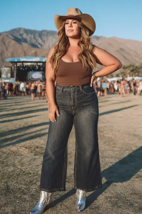 a confident plus size woman at the Stagecoach country music festival, wearing a fitted brown tank top, high-waisted dark wash flare jeans, metallic silver cowboy boots