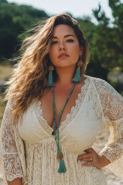plus size woman standing outdoors in nature, wearing a cream lace bohemian maxi dress with long bell sleeves and a deep v neckline, turquoise tassel earrings