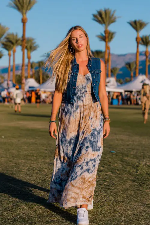 tall slim woman walking through Coachella festival grounds in the desert, wearing a blue and beige tie-dye maxi dress with a sleeveless denim vest, white sneakers (2)