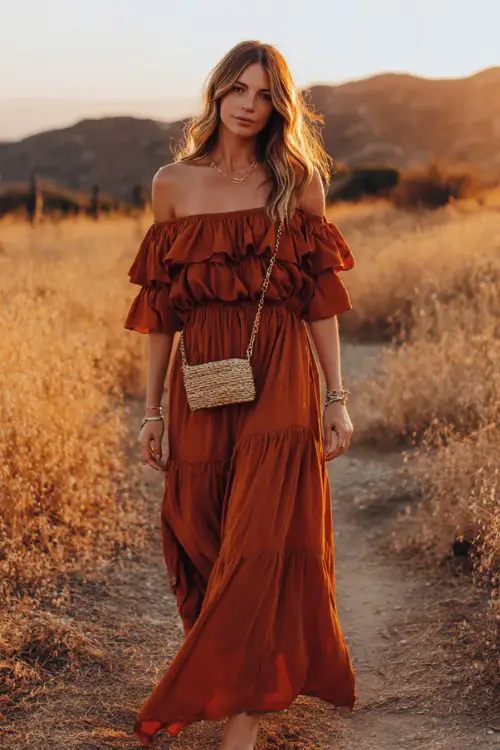 woman wearing a burnt orange off-shoulder flowy maxi dress with ruffled sleeves and cinched waist, straw crossbody bag with chain strap