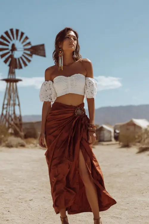 woman wearing a white lace off-shoulder crop top paired with a rust brown high-waisted wrap skirt with flowing fabric