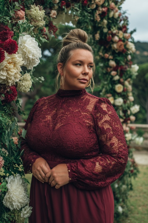 A plus-size woman over 50 wearing a burgundy lace midi dress with a high neckline and sheer long sleeves, standing by a grand floral wedding arch