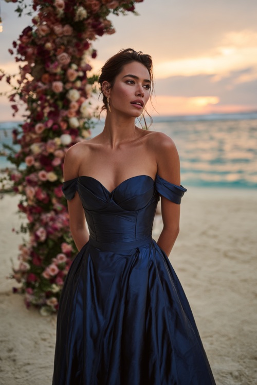 A woman in a navy blue floor-length satin gown with a structured bodice and off-the-shoulder sleeves, posing near a grand floral arch at a sunset beach wedding