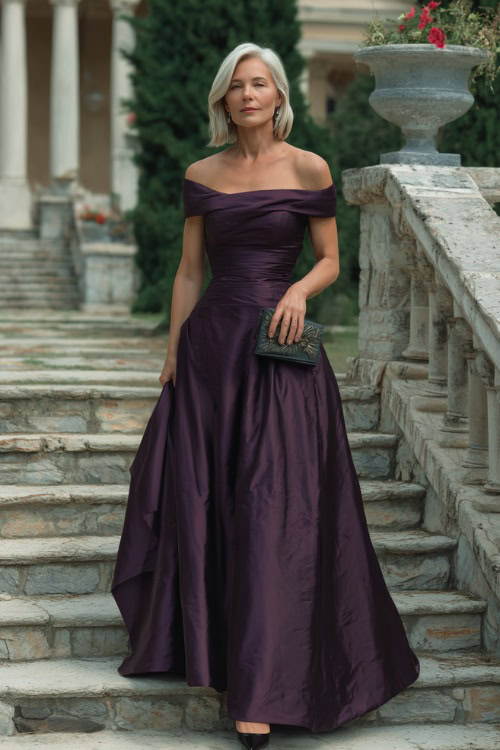 A woman over 50 in a deep plum evening gown with off-the-shoulder sleeves and a floor-length skirt, standing on the steps of a formal outdoor wedding venue 